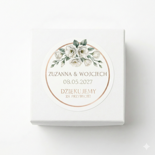 Białe pudełeczko na upominki dla gości weselnych z okrągłą personalizowaną naklejką. Elegancki wzór ślubny z motywem białych kwiatów, zielonych liści i ramką w odcieniu różowego złota. Widoczne imiona pary młodej oraz data ślubu.