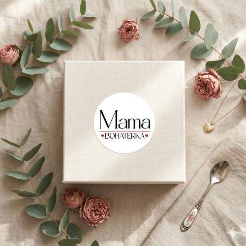 Białe lniane pudełko prezentowe na beżowym tle, ozdobione okrągłą naklejką z napisem Mama Bohaterka i małymi czerwonymi serduszkami. Nowoczesne i eleganckie opakowanie na Dzień Matki.