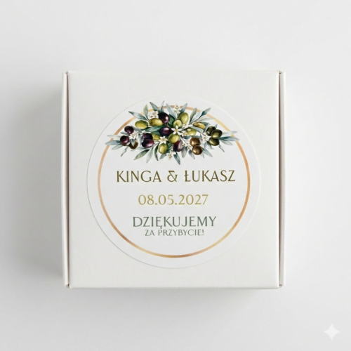 Białe kwadratowe pudełeczko na prezenty dla gości weselnych. Na wierzchu okrągła personalizowana naklejka ślubna w stylu toskańskim z motywem gałązek oliwnych, zielonymi oliwkami i złotą ramką, z imionami pary młodej oraz datą wesela.